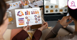 Equipo de trabajo analizando gráficos e infografías impresas junto a una laptop con reportes estratégicos en una mesa de oficina.